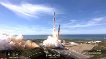 Rocket launching with flames and smoke against a clear blue sky.