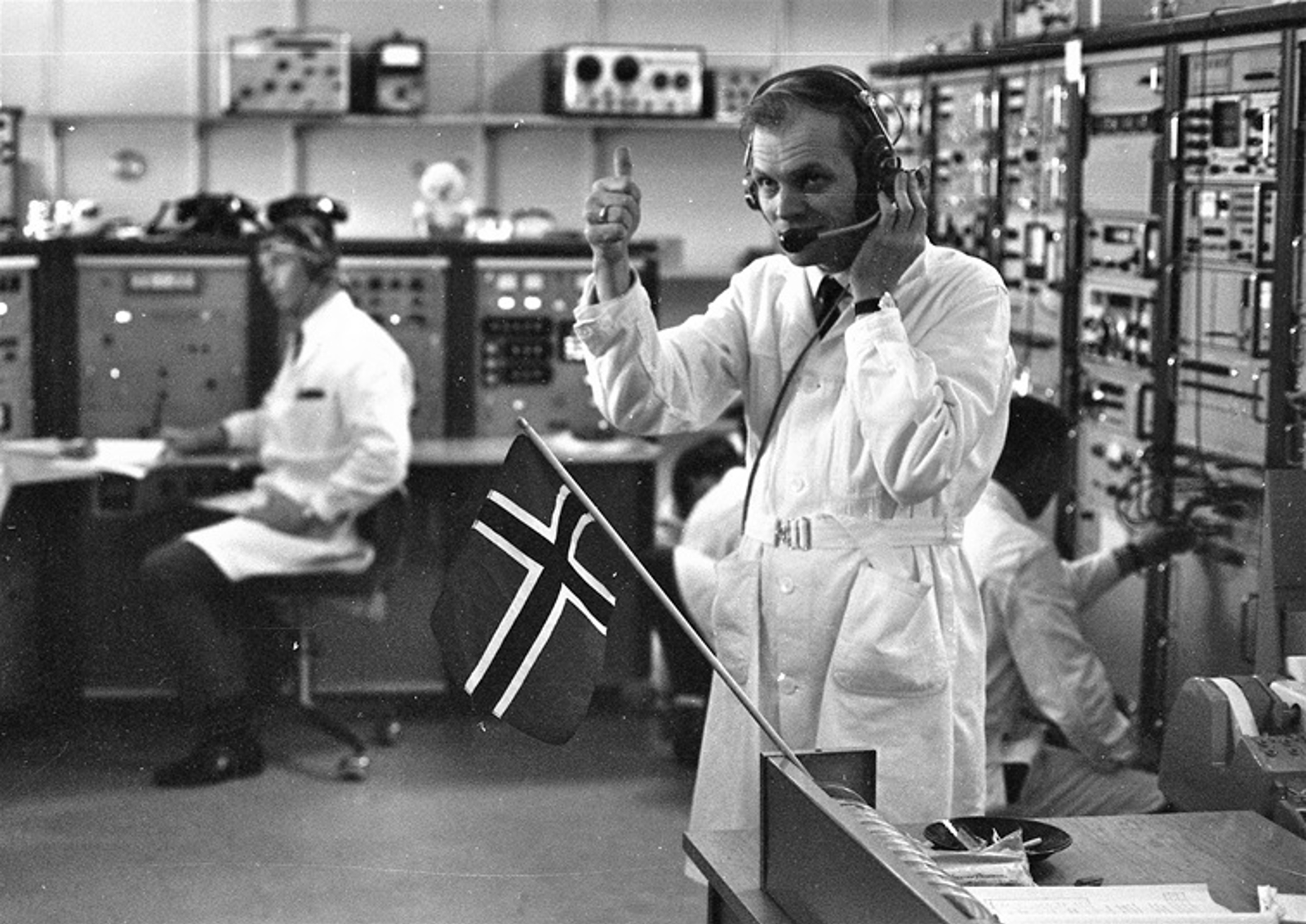 Scientists in lab coats working with large control panels and equipment.