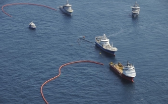 Ships in the ocean with floating barriers, conducting an oil spill cleanup.