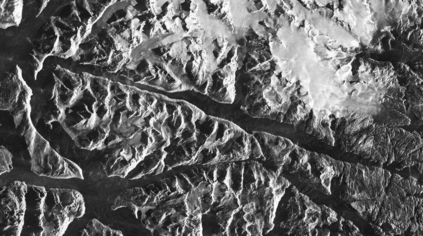 Aerial view of rugged, mountainous terrain with snow-covered peaks.