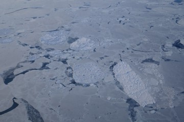 Aerial view of broken ice floes floating on a grey sea.