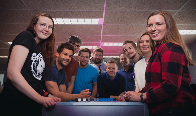 A group of ten people smiling and posing together indoors, with a ceiling light in the background.