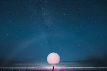 A person standing in front of a large geodesic dome under a starry night sky.