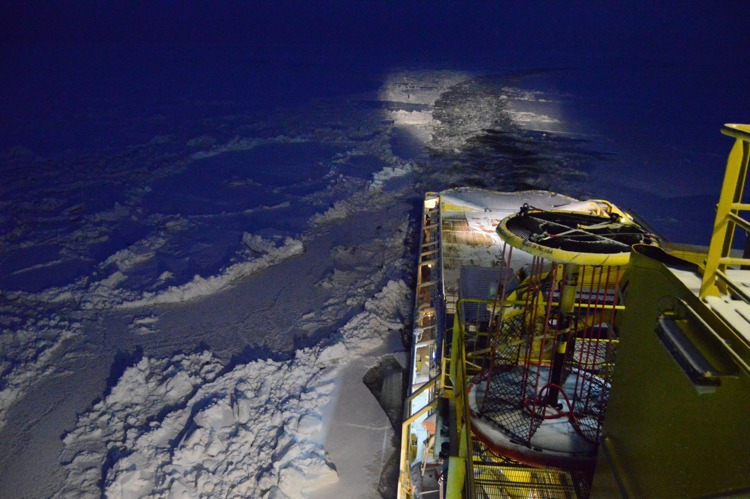 A ship navigating through ice-covered waters at night, with lights illuminating the icy path.