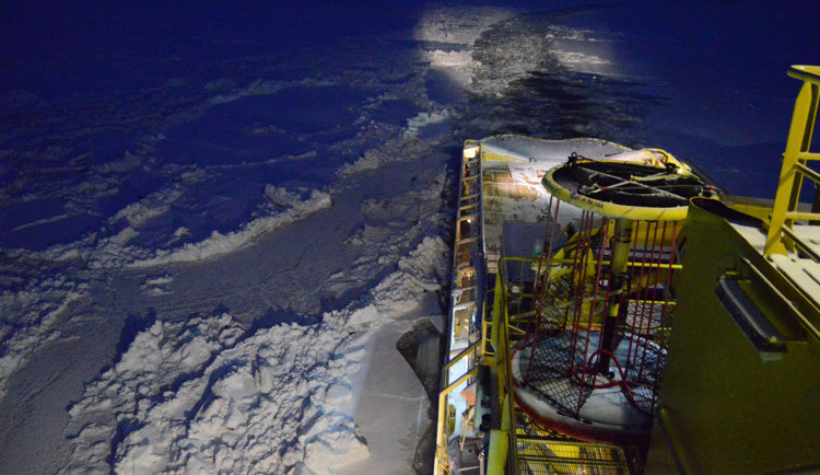 Ship breaking through ice in the dark with illuminated deck and ice-covered surroundings.