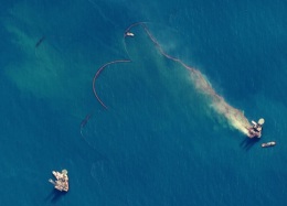 Aerial view of an offshore oil spill with visible containment efforts and boats in the surrounding water.